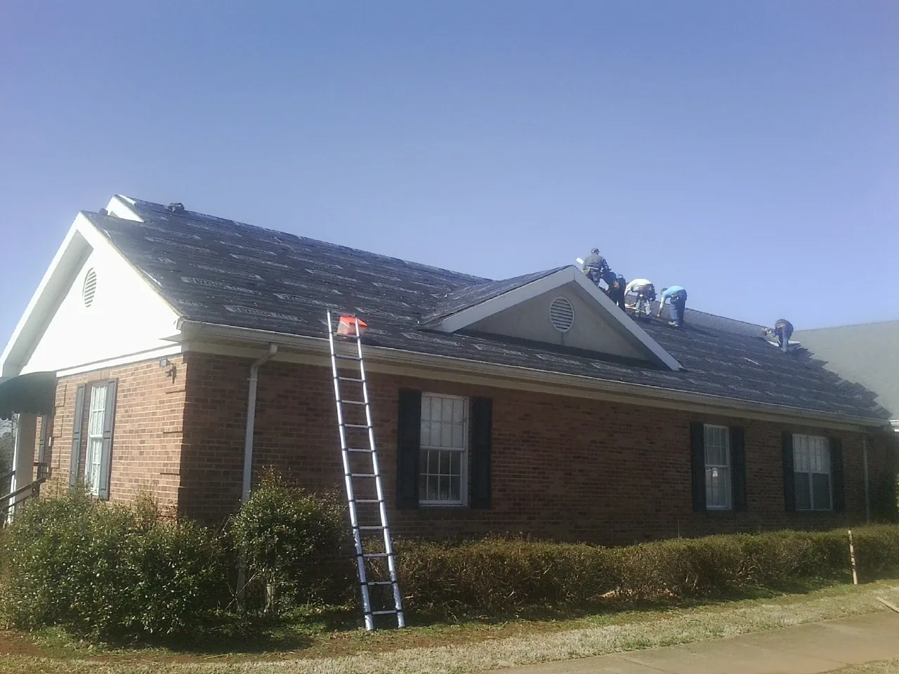 Crew tearing shingles off a brick ranch roof with a ladder set — Emergency Roof Repair work by our crew in Cawood