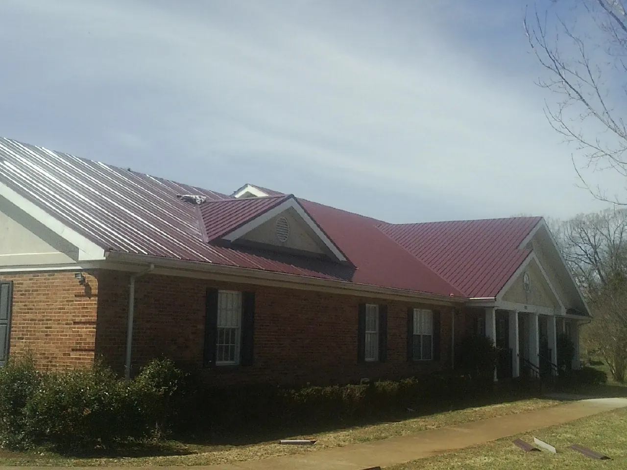 Red metal roof with gabled entries on a long brick building, from a Hail Damage Roof Repair job in Cawood