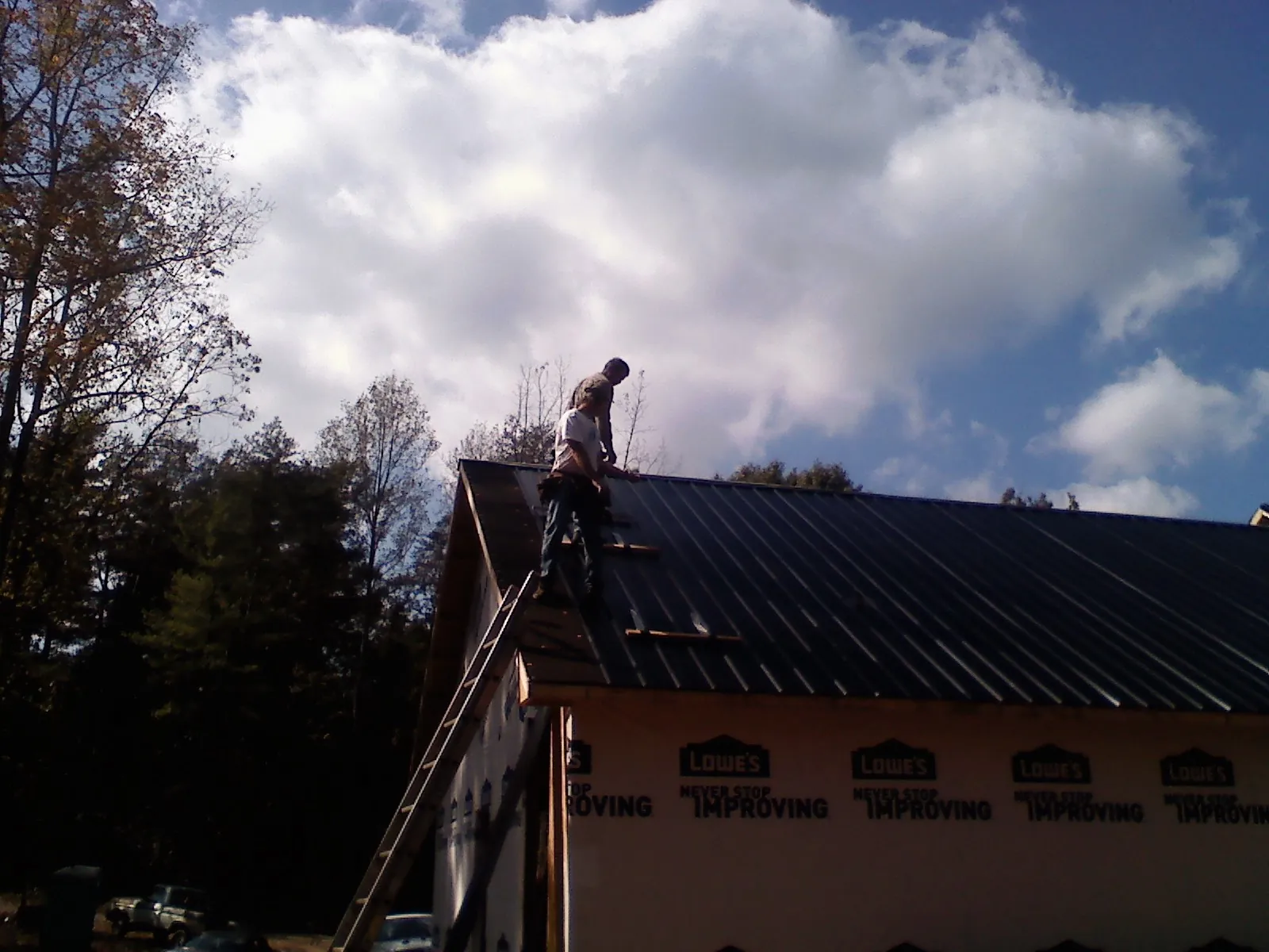 Roofer fastening dark metal panels high against a cloudy sky, from a Roof Inspection job in Cawood