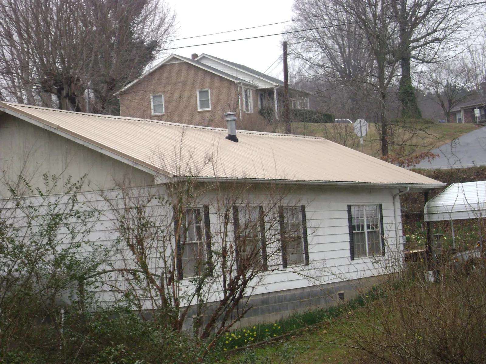 Tan metal roof on a white sided house set into a hillside — Commercial Roofing by Roofing Brothers in Cawood